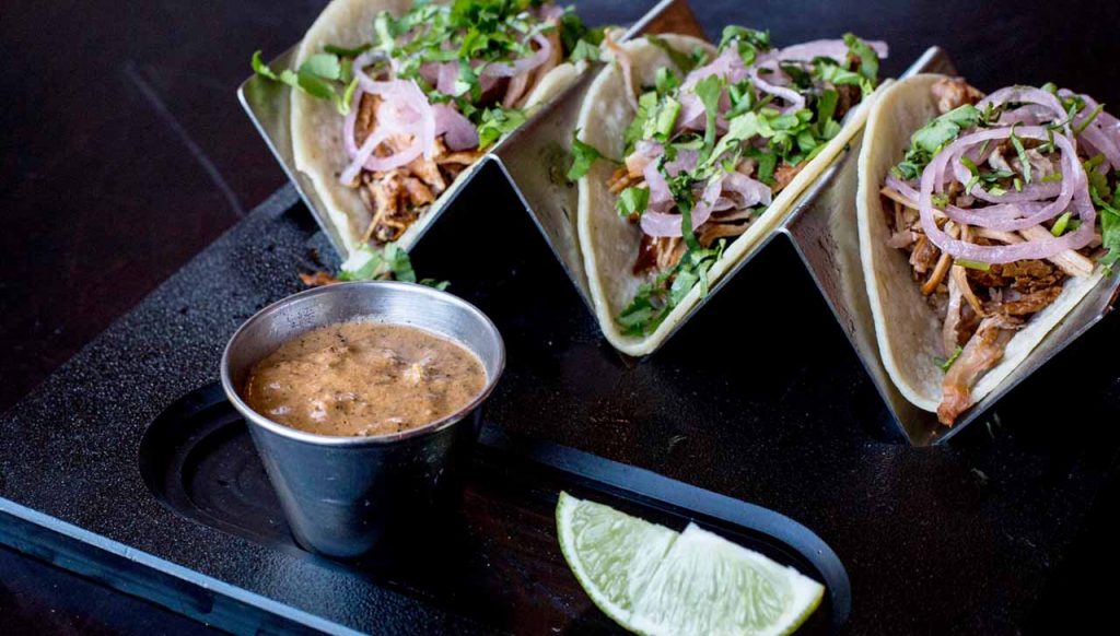 Three pork tacos with dipping sauce from Que Onda